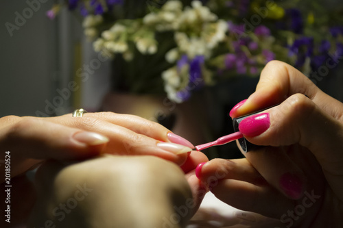 Manicure nail paint. Beautician applying nail polish to female nail in nail salon. Closeup photo