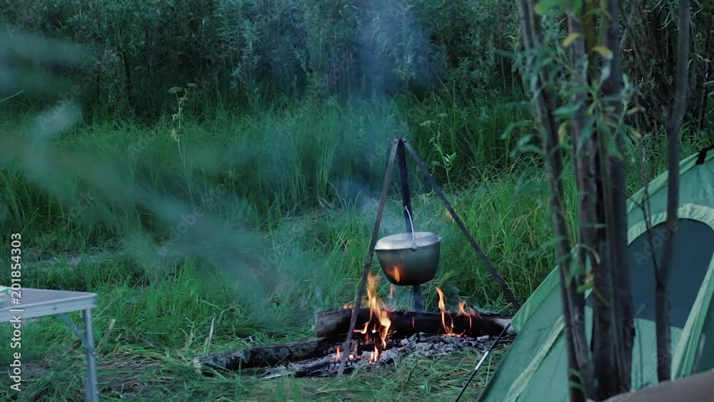 A bonfire in the clearing A bonfire with a bowler on the tripod between the table and the tent in general A bonfire in the clearing A bonfire with a bowler on the tripod between the table and the tent in general