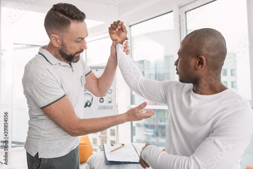 Medical consultation. Serious professional therapist holding his patients arm while looking at it