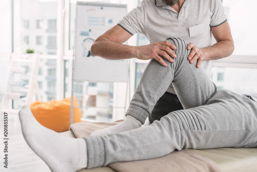 Fototapeta premium Physical trauma. Close up of a male leg being bend during the rehabilitation therapy procedure