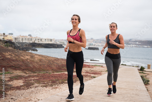 Smiling young women running by the seaside