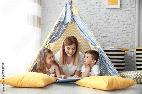 Nanny and little children reading book in tent at home photo