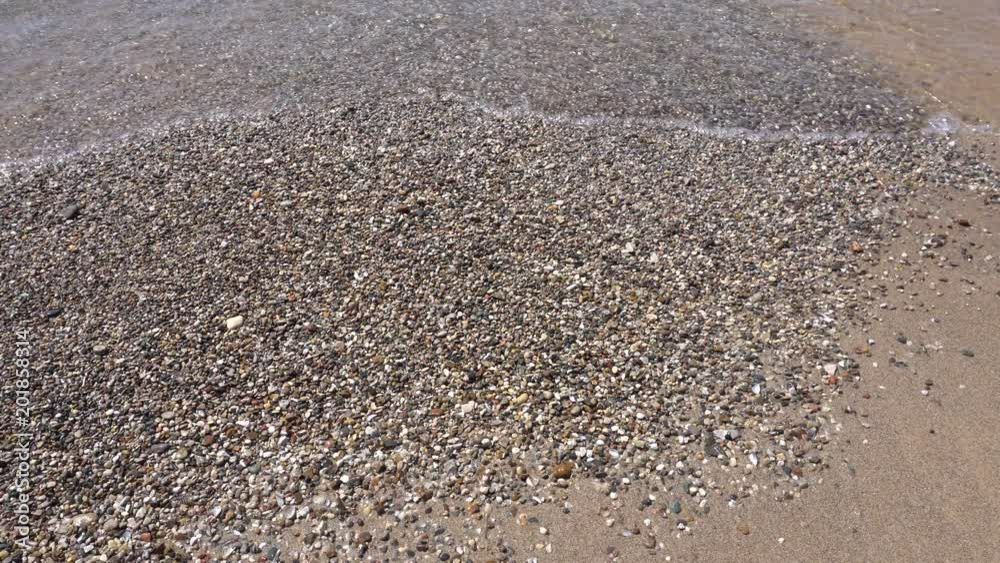 Water washing on shore over pebbles and beach on bright sunny day Water washing on shore over pebbles and beach on bright sunny day