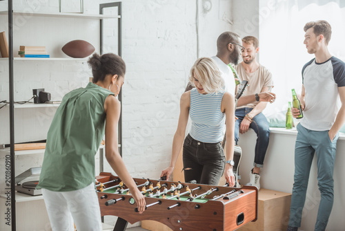 young women playing table football with male friends standing behind