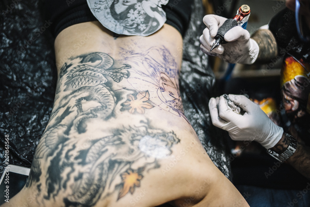 Master tattooing a back woman