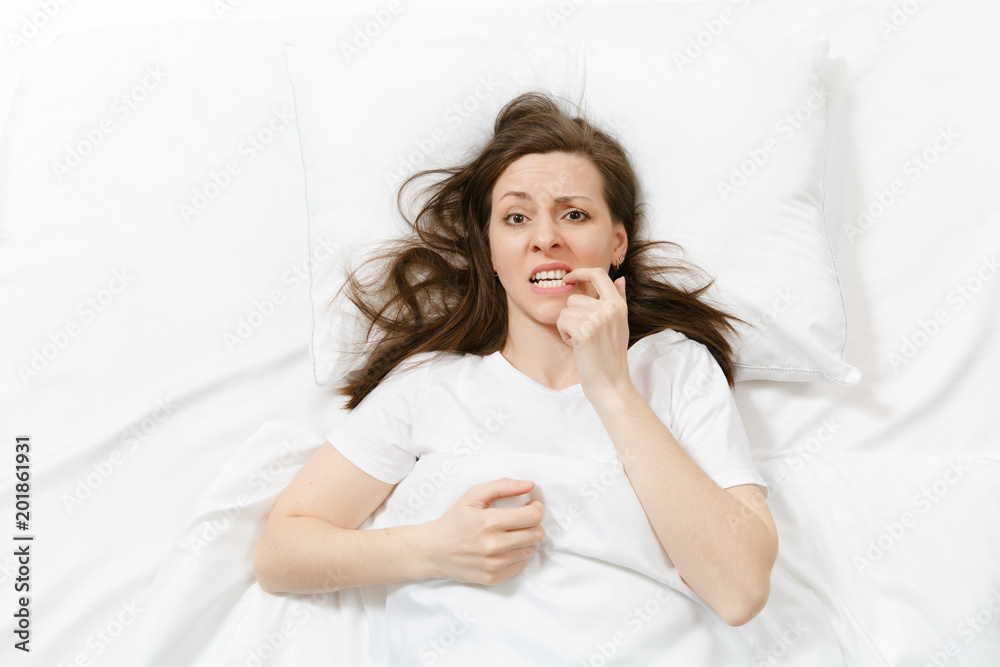 Top view of tired stressed crying young woman lying in bed with white sheet, pillow, blanket. Pensive frustrated sad upset female spending time in room. Rest, relax, bad mood concept. Copy space. Top view of tired stressed crying young woman lying in bed with white sheet, pillow, blanket. Pensive frustrated sad upset female spending time in room. Rest, relax, bad mood concept. Copy space.