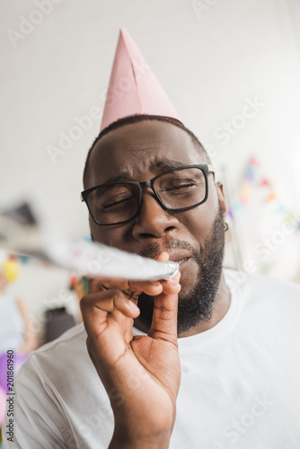 Happy african american in party hat blowing party horn photo