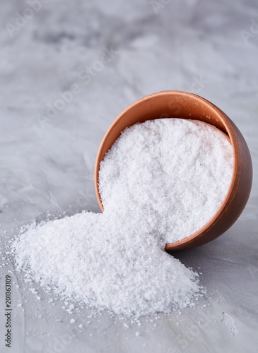Composition of sea salt in ceramic bowl and spoon for cooking or spa on white background, top view, selective focus