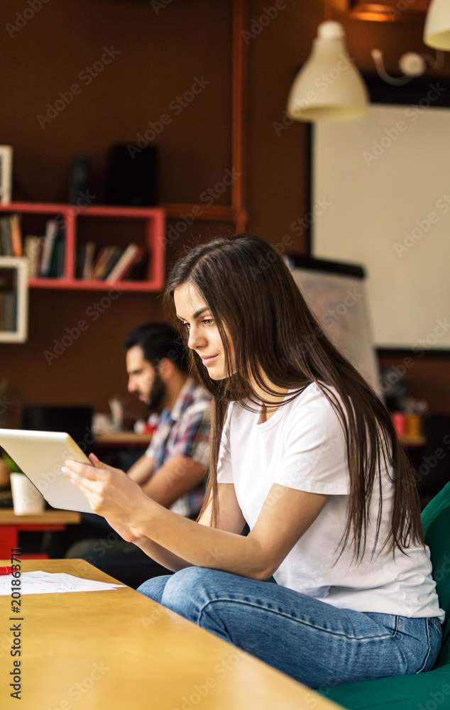 Brunette girl working with tablet computer sitting in coworking cafe office Brunette girl working with tablet computer sitting in coworking cafe office