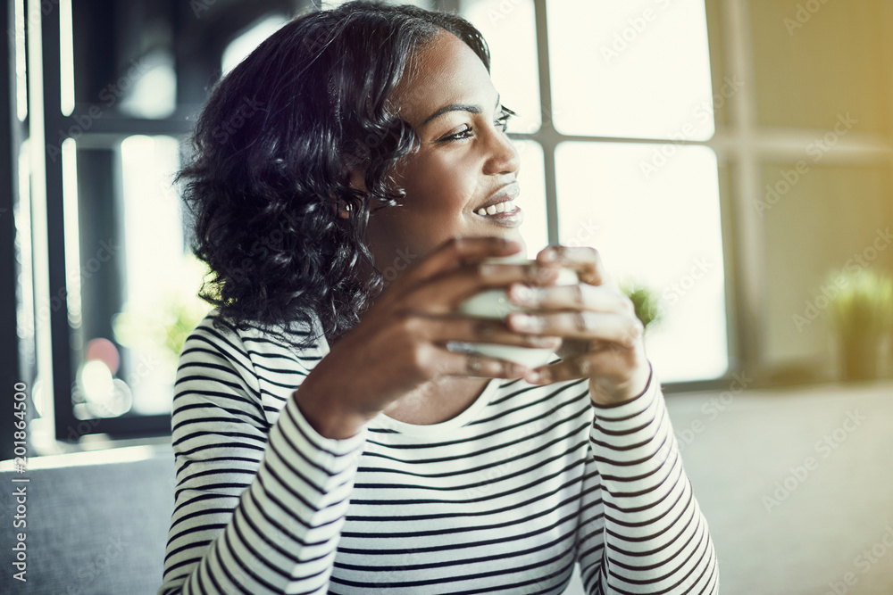 Smiling African woman looking through a window and drinking coff Smiling African woman looking through a window and drinking coff