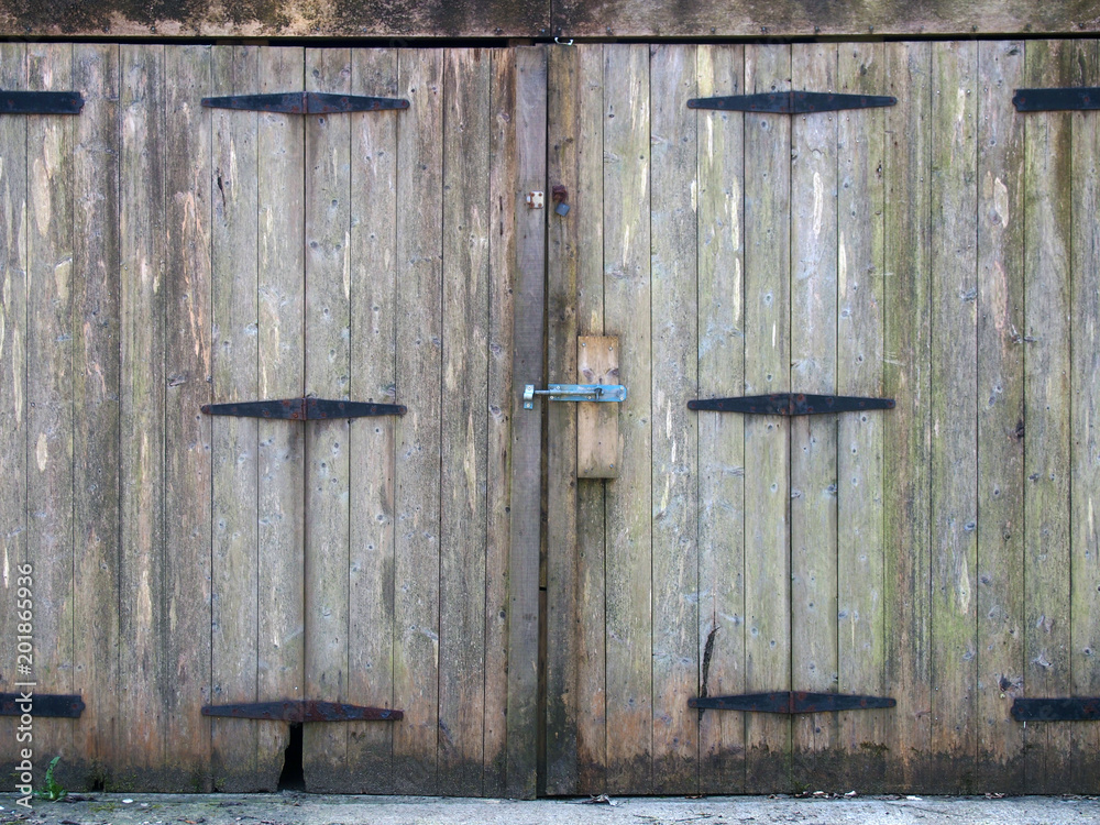 old rural grey plank wooden plank doors with a bolt fastening and rusty iron hinges