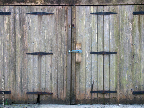 old rural grey plank wooden plank doors with a bolt fastening and rusty iron hinges