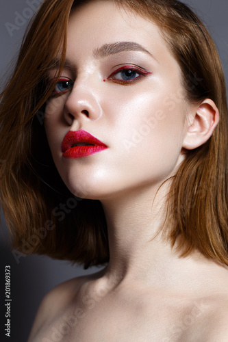 Young girl with red lips and red arrows in front of eyes. Beautiful model with makeup nude and shining skin. Photo taken in the studio. Beauty of the face. Female portrait. 