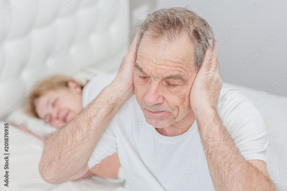 Senior man plugged his ears and can not sleep because his wife snores Senior man plugged his ears and can not sleep because his wife snores