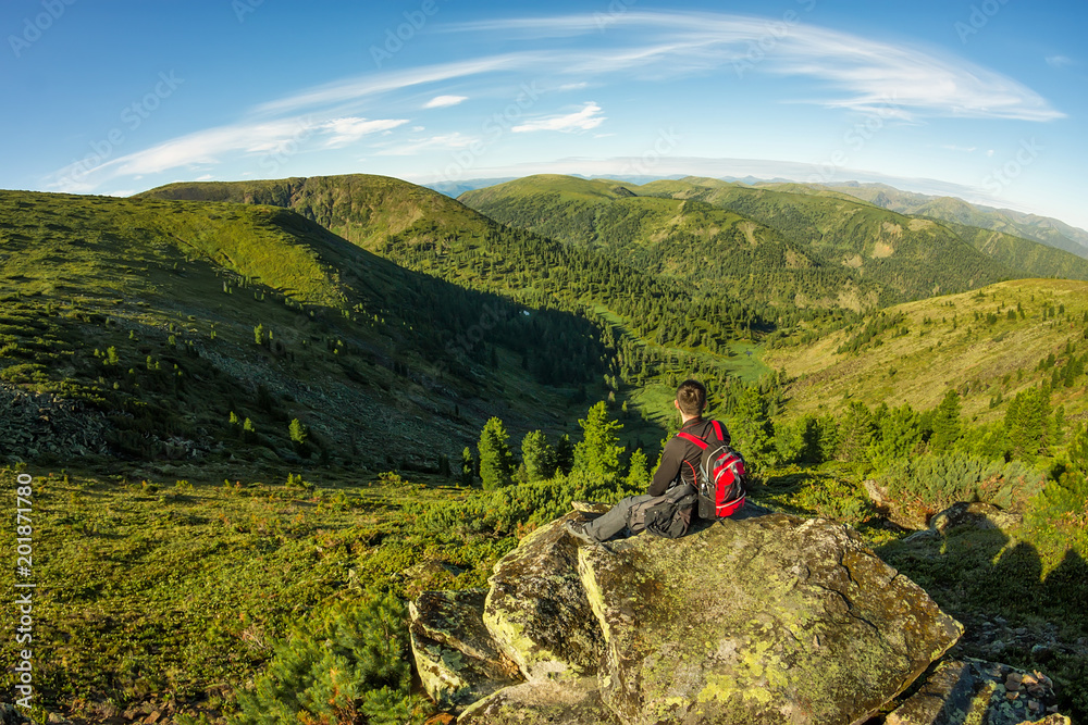 young man with a backpack sits on a rock in the mountains view