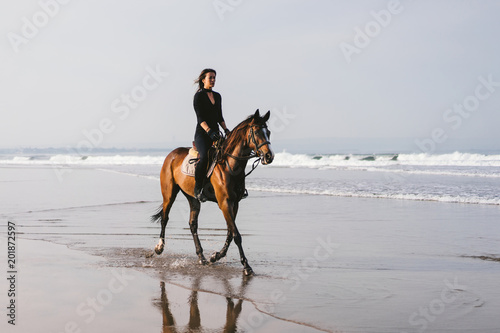 young female equestrian riding horse near wavy ocean