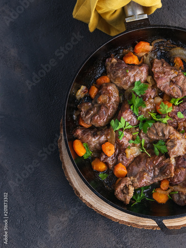 Stewed pork cheeks with vegetables in an iron pan, with a dark background on an overhead shot. Spanish food. Copy space.