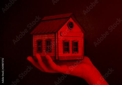 Fotografija Small toy house in a hand on a dark red background