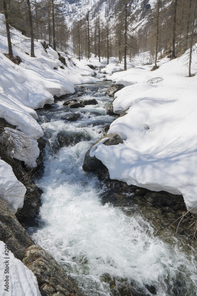 Alpine valley with snow in spring, creek swollen by thaw