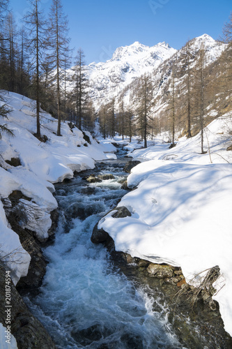 Alpine valley with snow in spring, creek swollen by thaw