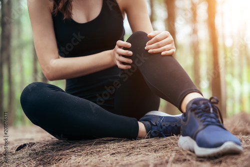 Asian girl is exercising at the weekend and she is tying shoelaces in a pine forest green and lush beautiful. Sport girl and lifestyle concept. Her knee injury from exercise.