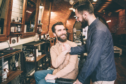 Two guys are shaking each other's hands. Tey are happy to meet in a barbershop.