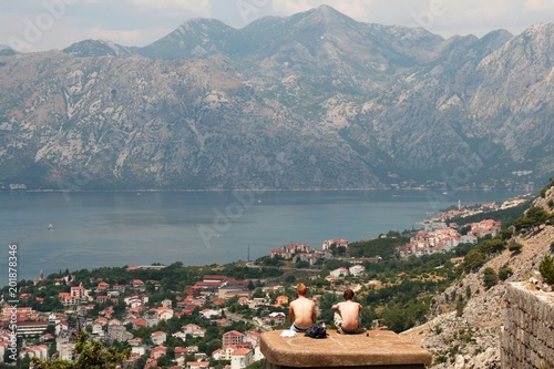 men traveles sitting on the top roof  and observing Kotor old city, gulf,  mountains in the sunny summer day photo