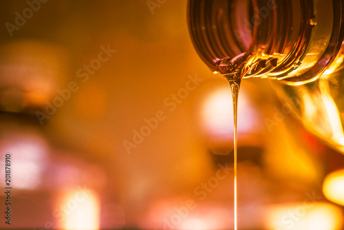 Liquid stream of motorcycle motor oil flows from the neck of the bottle close-up.