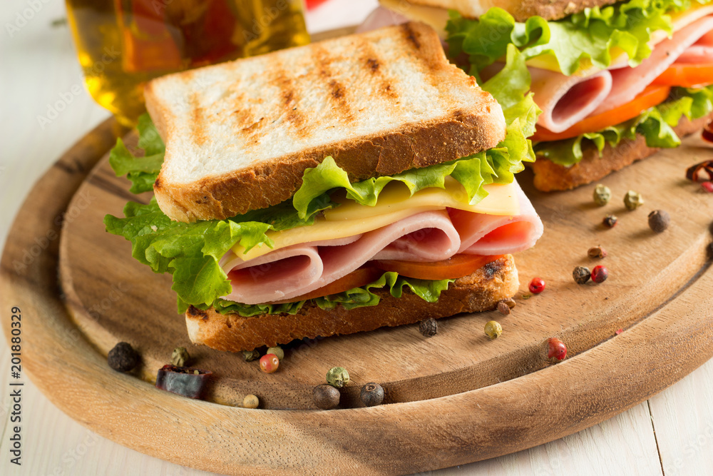 Close-up photo of a club sandwich. Sandwich with meet, prosciutto, salami, salad, vegetables, lettuce, tomato, onion and mustard on a fresh sliced rye bread on wooden background. Olives background.