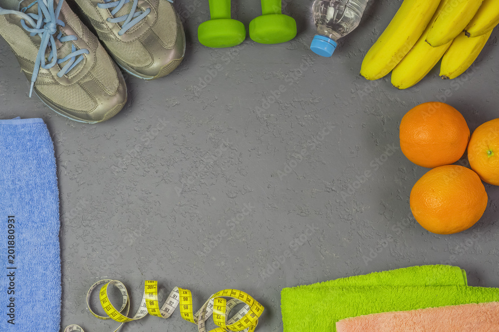 on a gray background sports equipment, water, dumbbells and fruit on a gray background sports equipment, water, dumbbells and fruit