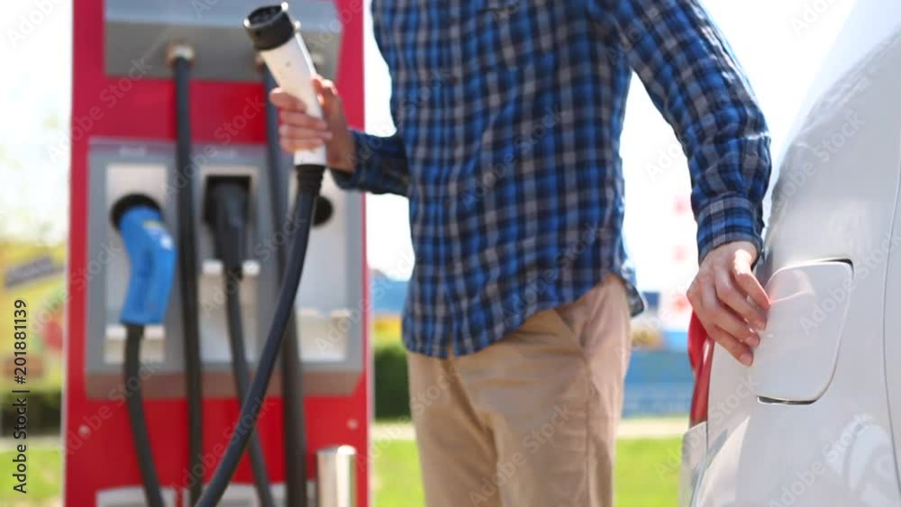 A man at the charging station for electric vehicles pulls out the plug from car the socket