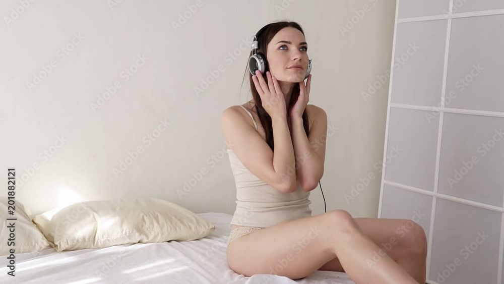 girl sitting on a bed in the bedroom and listens to music with headphones girl sitting on a bed in the bedroom and listens to music with headphones