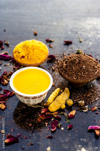 Ayurvedic face pack of chandan,Haldi, and gulab jal or gulab ka pani, with raw turmeric, sandal wood powder and rose petals on wooden surface for good and natural bright, white skin. photo