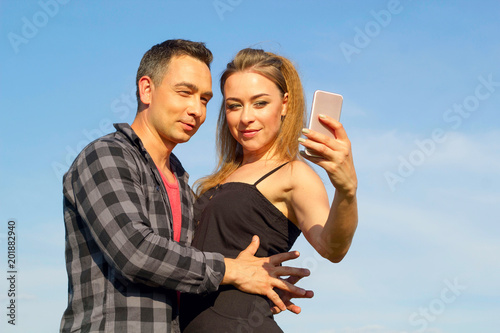 Two Young beautiful man and woman in casual clothes making selfie over blue sky