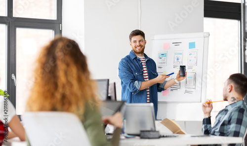business, technology and people concept - man showing smartphone user interface design to creative team at office presentation