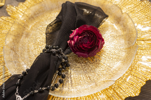 The bud of a red rose, lying on a golden plate, next to a black veil, girded with a necklace