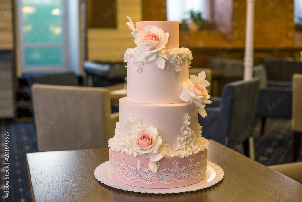 Fototapeta premium Beautiful elegant four tiered pink wedding cake decorated with roses flowers. Concept floral from sugar mastic