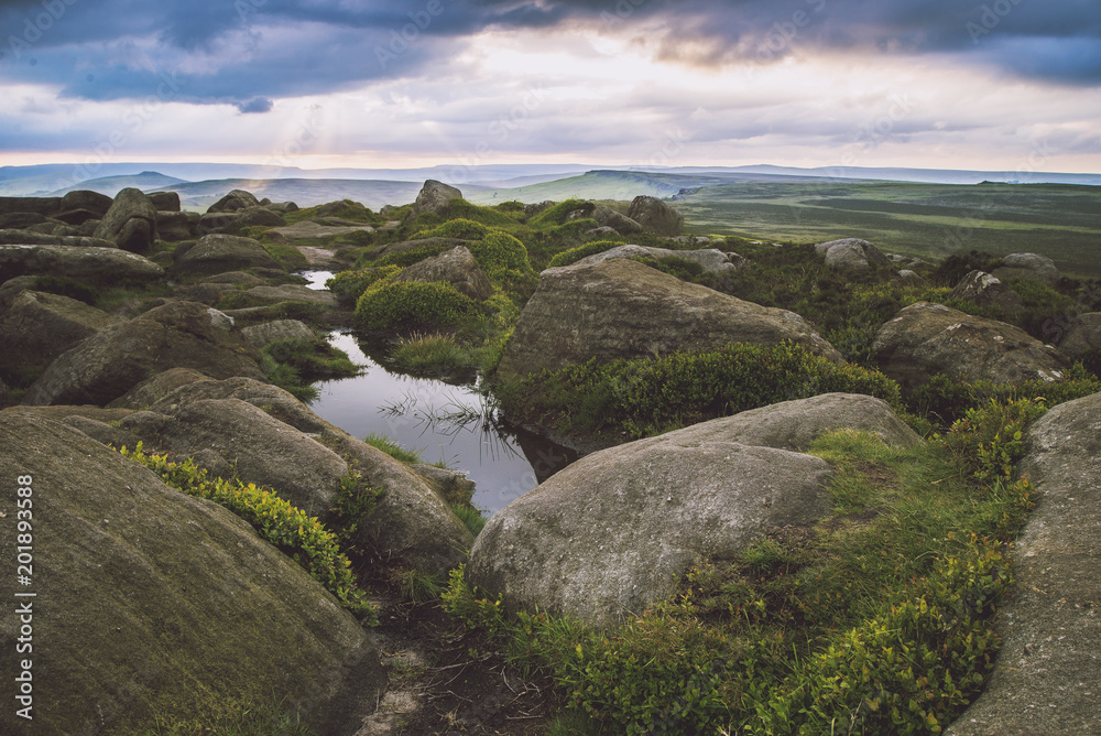 Sun bursting through clouds over rocky green landscape