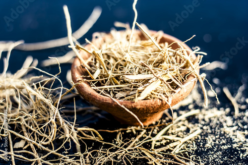Dried vetiver grass or khus or Chrysopogon zizanioides grass in a clay bowl on wooden surface. photo