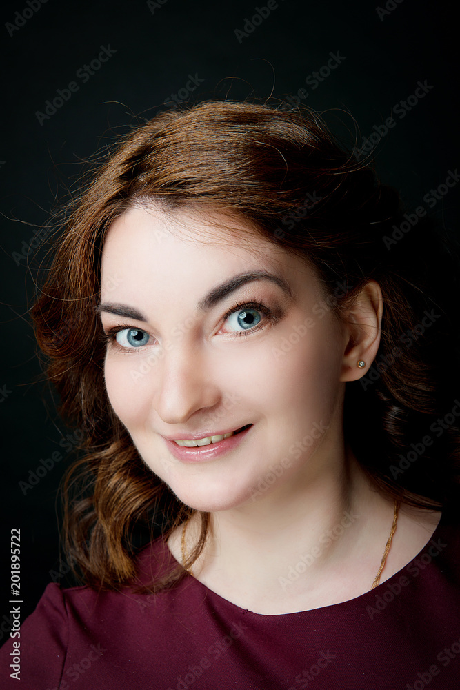 Naklejka premium A brunette girl with a smile on her face against a black background. Studio portrait of a woman.