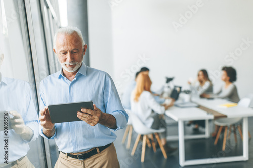 Senior businessman standing by window with digital tablet in his hand