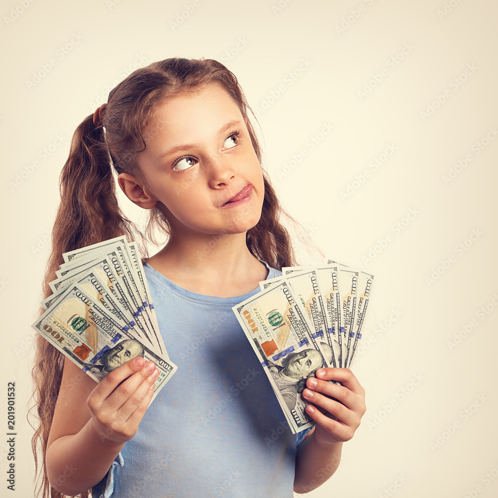 Happy grimacing fun thinking kid girl holding money in the hands and looking up on empty copy space. Toned portrait vintage Happy grimacing fun thinking kid girl holding money in the hands and looking up on empty copy space. Toned portrait vintage