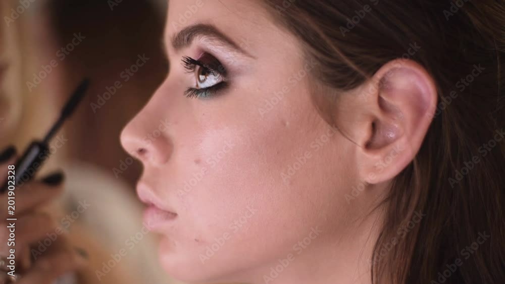 Make-up artist applying the mascara to model. Close up. Makeup artist doing makeup for girl indoor. Make-up artist applying bright base color eyeshadow on model's eye. Make-up artist applying the mascara to model. Close up. Makeup artist doing makeup for girl indoor. Make-up artist applying bright base color eyeshadow on model's eye.