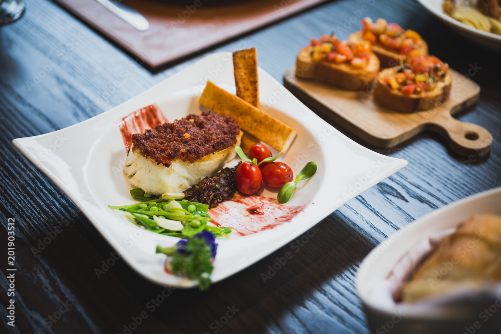 Baked Cod fish with sauce, pan grilled baby vegetables, pea and tomato served with bread sticks. Baked Cod fish with sauce, pan grilled baby vegetables, pea and tomato served with bread sticks.
