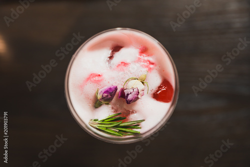 Red cocktail in wine glass topping with foam, flowers and rosemary.