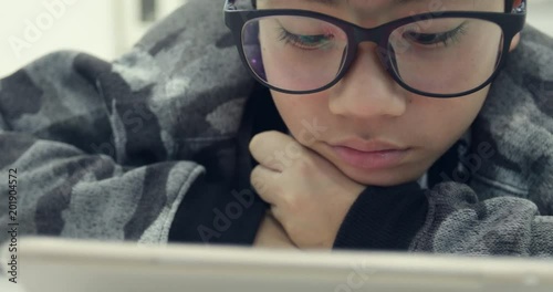 Cute asian boy wearing eyeglasses and using tablet computer ,Young teenage boy playing games on digital tablet .