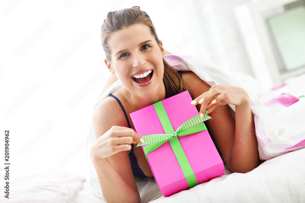 Young woman unpacking a surprise present in bed Young woman unpacking a surprise present in bed