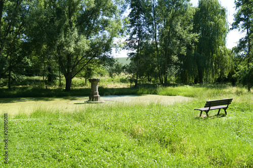 Altenburg / Germany: Idyllic bench at the so called „Fairytale Fountain“, a small pond with the remains of a historic drinking trough for horses on the outskirts of the former residential city photo