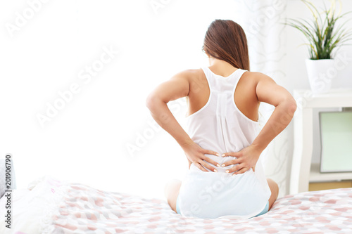 Young woman waking up in bed with backache photo
