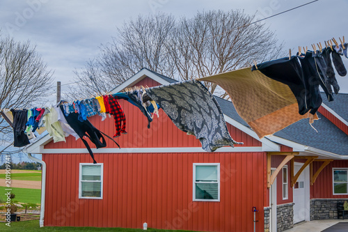 Outdoor view of clothes of Amish drying in the sun and air after laundry with a wooden red house background in Lancaster